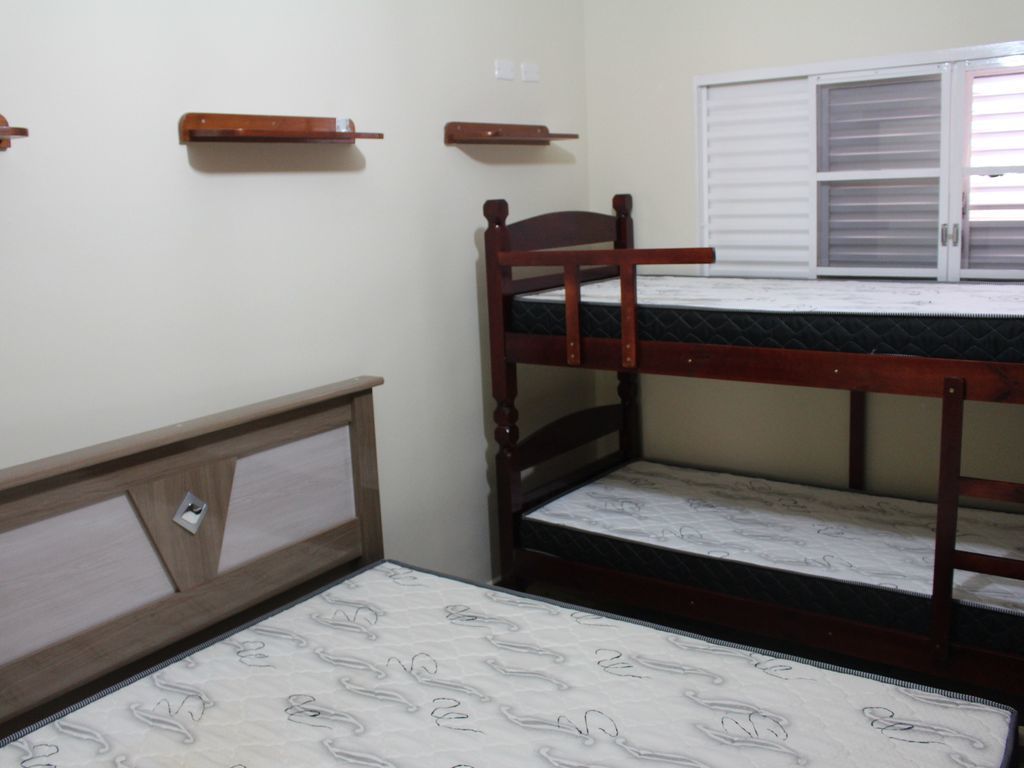Una cama individual con estructura de madera y un colchón con funda estampada. Se observa una ventana con persianas a la derecha.