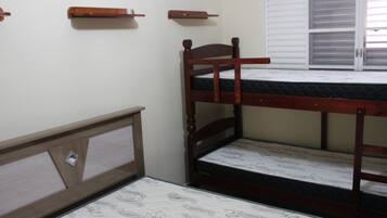 Una cama individual con estructura de madera y un colchón con funda estampada. Se observa una ventana con persianas a la derecha.