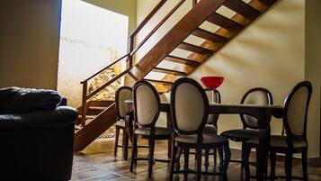 A dining area with a wooden staircase, a dining table with chairs, and a red bowl on the table.