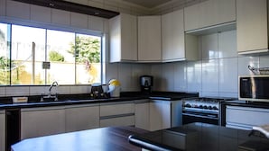 A modern kitchen with white cabinets, a black countertop, a stove, and a microwave. - Casa de Campo com Piscina Aquecida (Poços de Caldas)