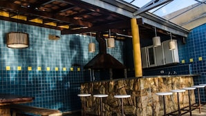 A bar area with a stone counter and stools, a wooden bench, hanging pendant lights, and a tiled wall. - Casa de Campo com Piscina Aquecida (Poços de Caldas)