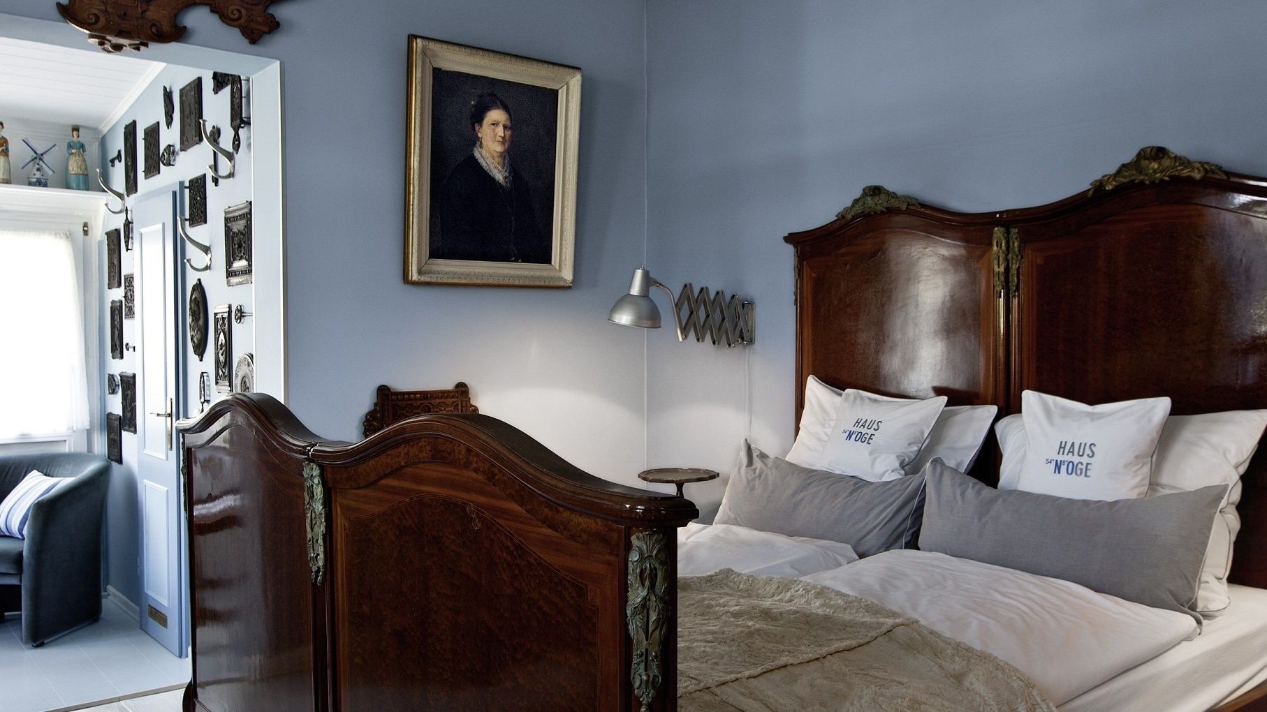 A bedroom with a wooden bed, a nightstand, and a dresser. There is a framed portrait on the wall and a lamp on the nightstand.