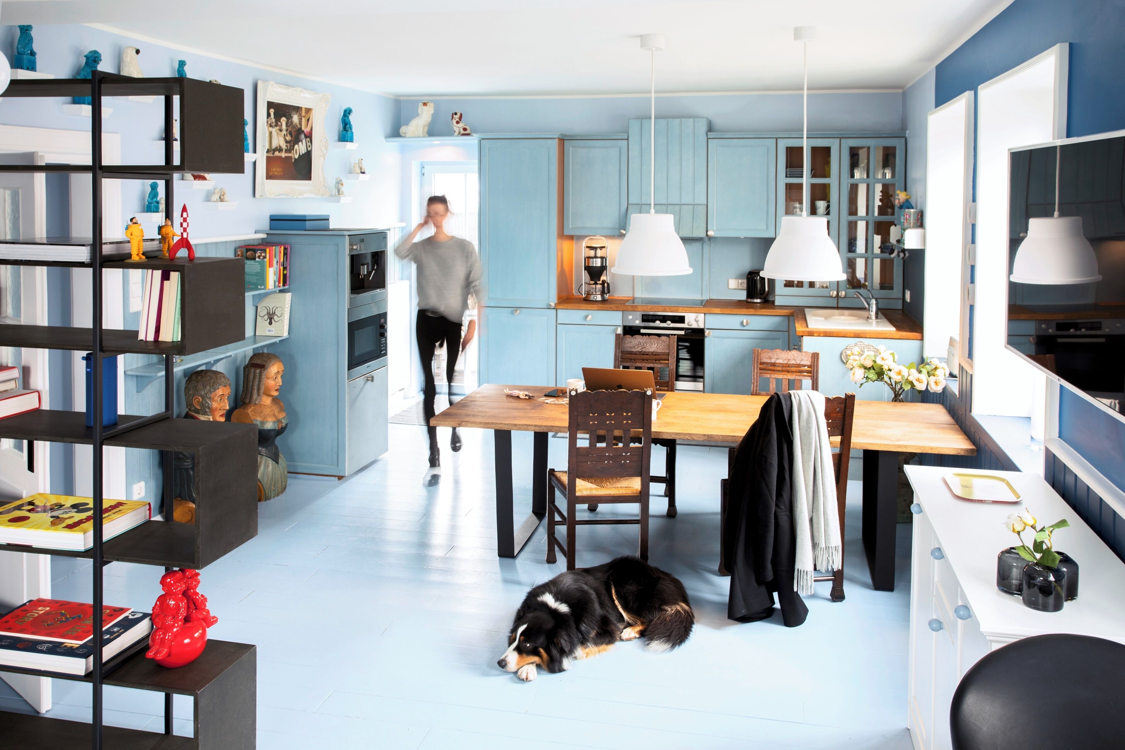 A modern kitchen with blue cabinets, a dining table, and a dog lying on the floor.
