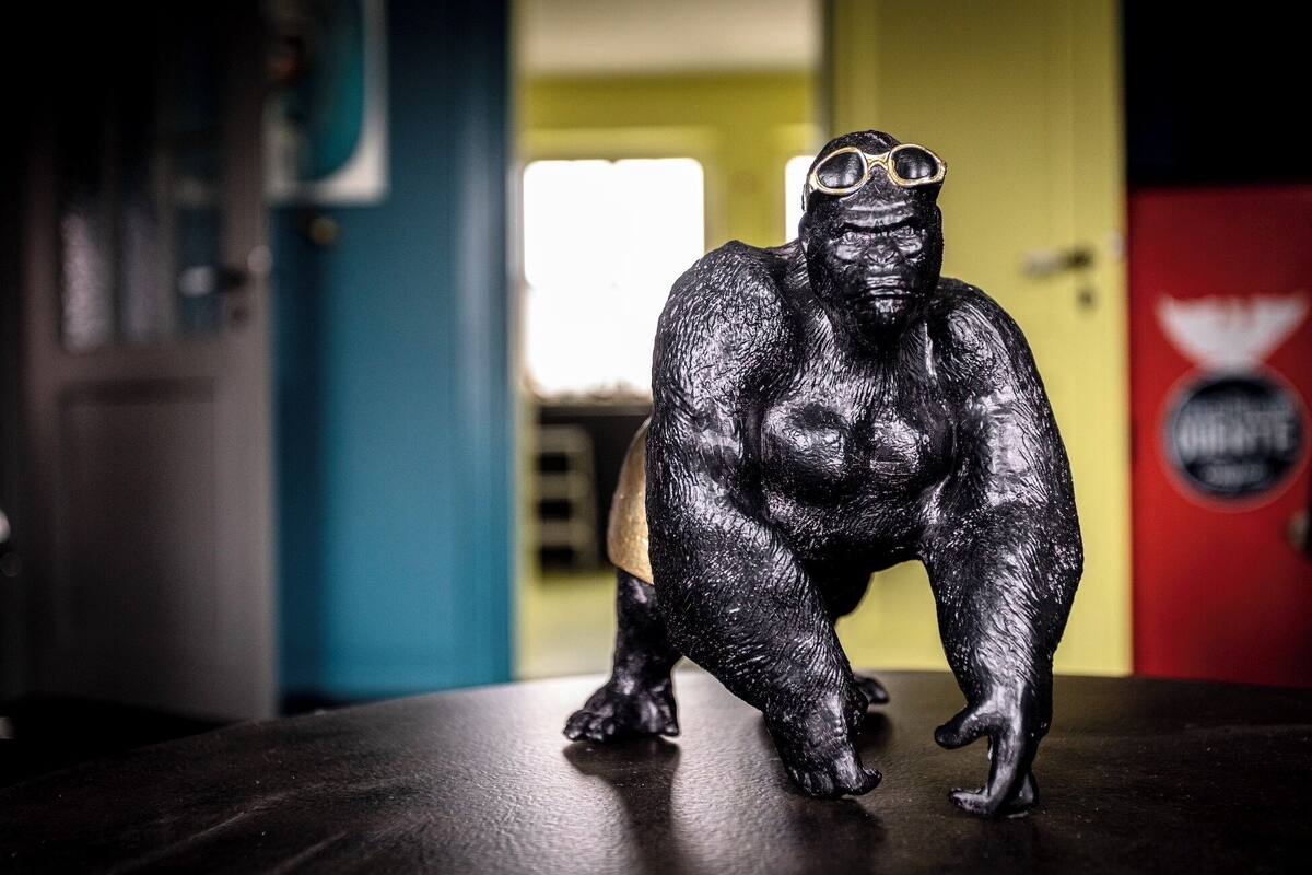 A black statue of a muscular figure with goggles on, placed on a table in a room with a blue wall and a red wall with a logo.