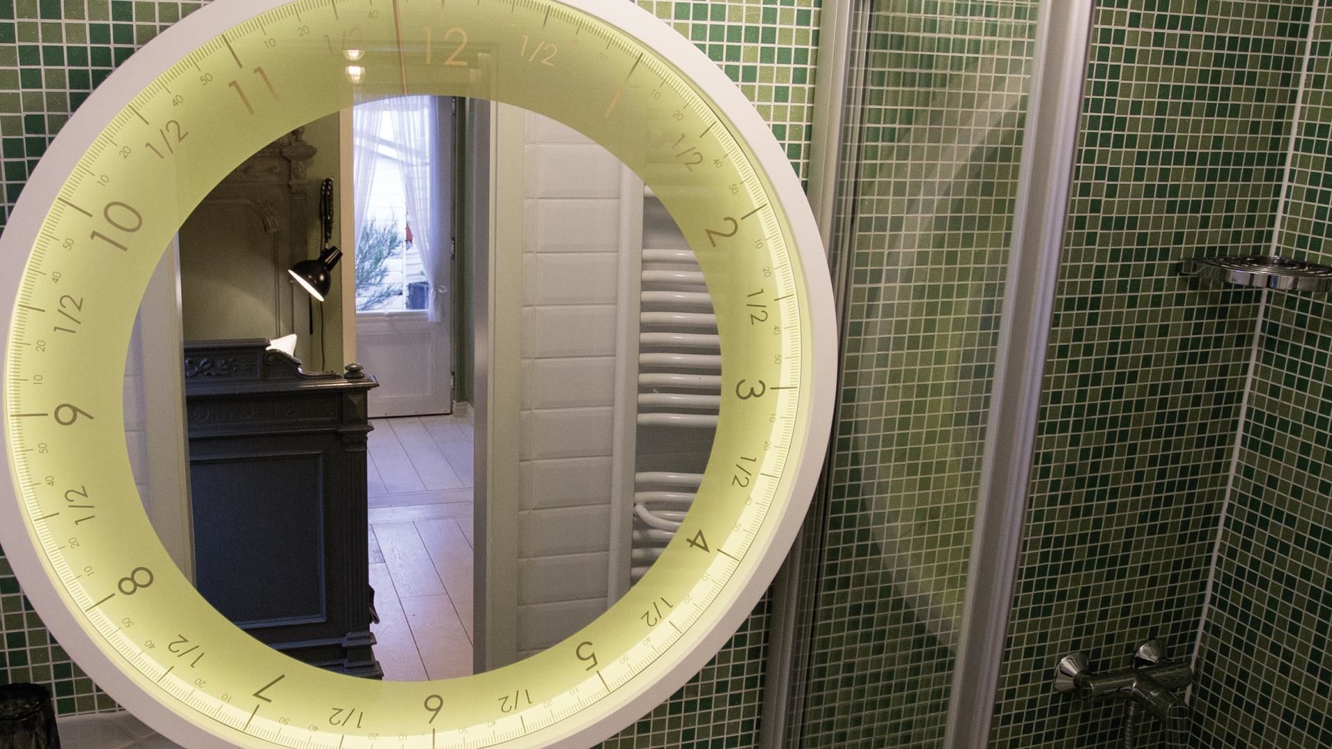 Un bagno con uno specchio circolare, pareti rivestite di piastrelle verdi e una zona doccia visibile.