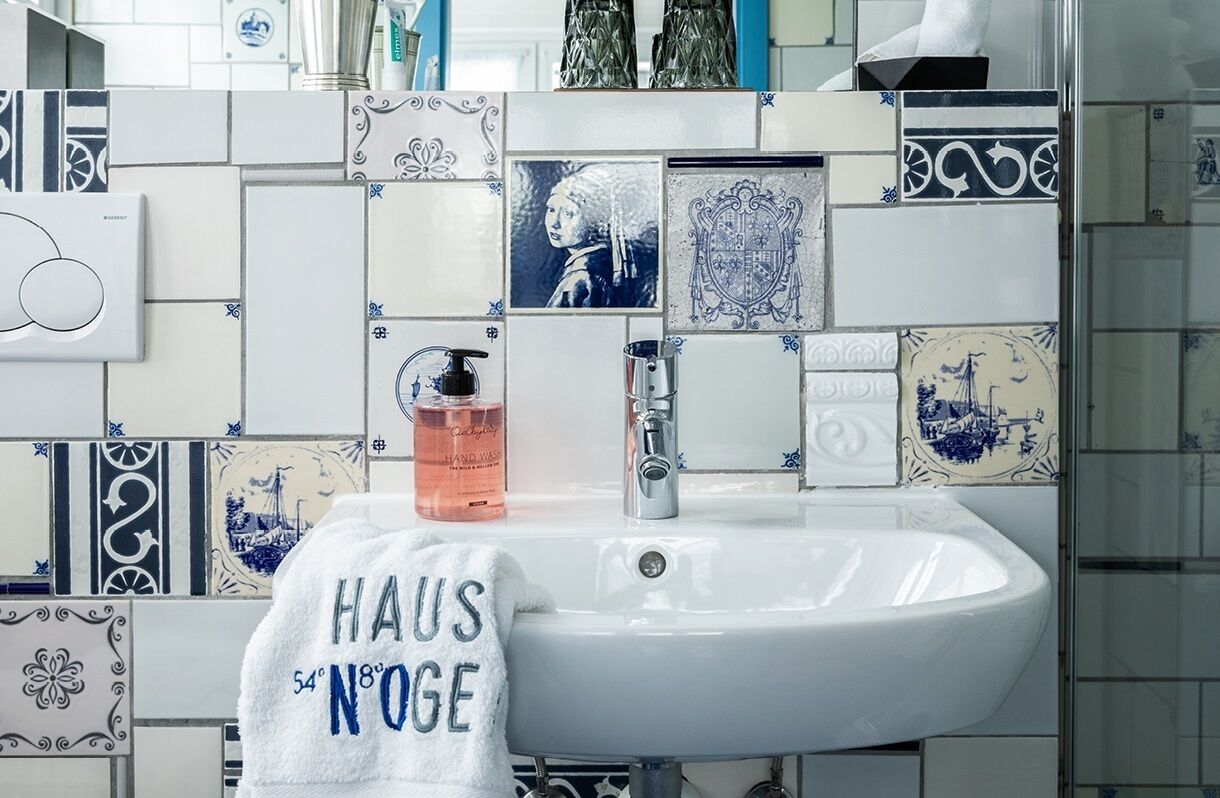 Un baño con un lavabo blanco, un dispensador de jabón para manos y una toalla con la inscripción "HAUS NOGE".