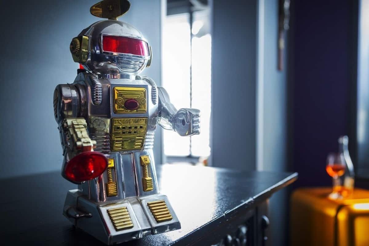 A metallic robot figurine on a table with a bottle and glass in the background.