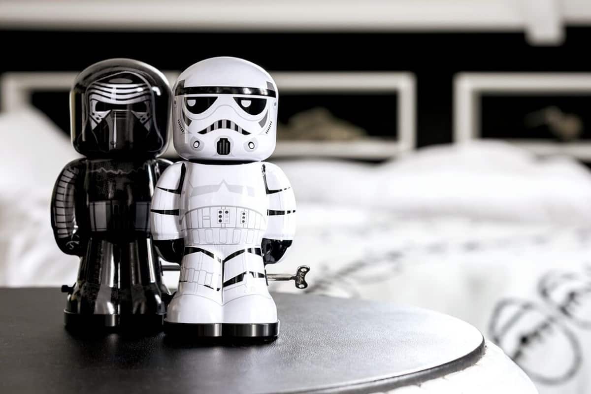 Two Star Wars figures on a table in a room with a bed and a TV in the background.