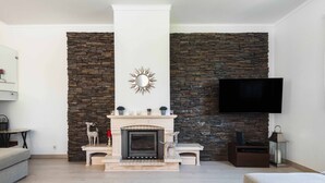 A living room with a stone fireplace, a mounted TV, and a sofa. - Sesimbra Stylish Villa by Homing (Sesimbra)