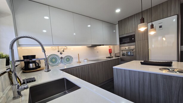 A modern kitchen with white cabinets, a stainless steel sink, a built-in oven, and pendant lighting. - Sesimbra Stylish Villa by Homing (Sesimbra)