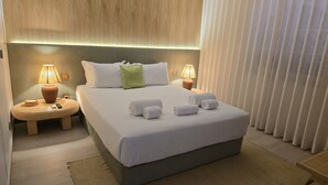 A neatly made bed with white linens and rolled towels, two bedside lamps, a green pillow, and a wooden headboard. - Sesimbra Stylish Villa by Homing (Sesimbra)