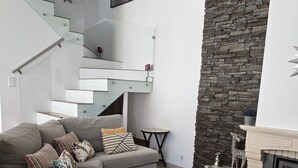 A modern living room with a grey sectional sofa, a fireplace, and a stone accent wall. - Sesimbra Stylish Villa by Homing (Sesimbra)