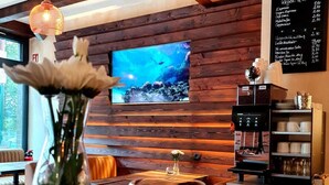 Interior de madera con una máquina de café, un tablero de menú y un televisor mostrando una escena submarina.