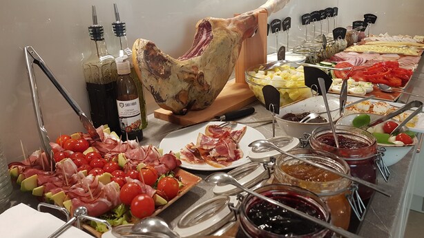 Un bufé con diversos alimentos, incluyendo carnes, quesos y salsas.