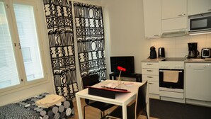 Une pièce de taille modeste comprenant un lit, une petite table, une chaise, un coin cuisine et un rideau à motifs.