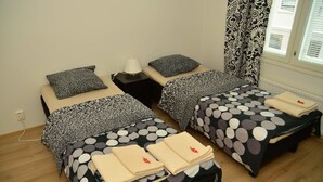Une chambre d’hôtel avec deux lits simples, chacun agrémenté d’une couvre-lit à motifs et de coussins assortis. On y trouve une table de chevet avec une lampe, ainsi qu’une fenêtre avec des rideaux à motifs.