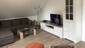 A modern living room with a sectional sofa, a glass coffee table, a flat-screen TV, a white cabinet, and a tall floor lamp.