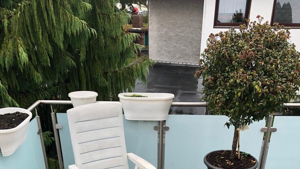 A wooden deck with a white chair and a small table. There is a potted plant and a white planter on the deck.