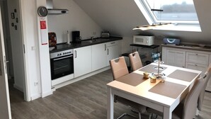 A modern kitchen with a skylight, white cabinets, a built-in oven, and a dining area with a table and chairs.