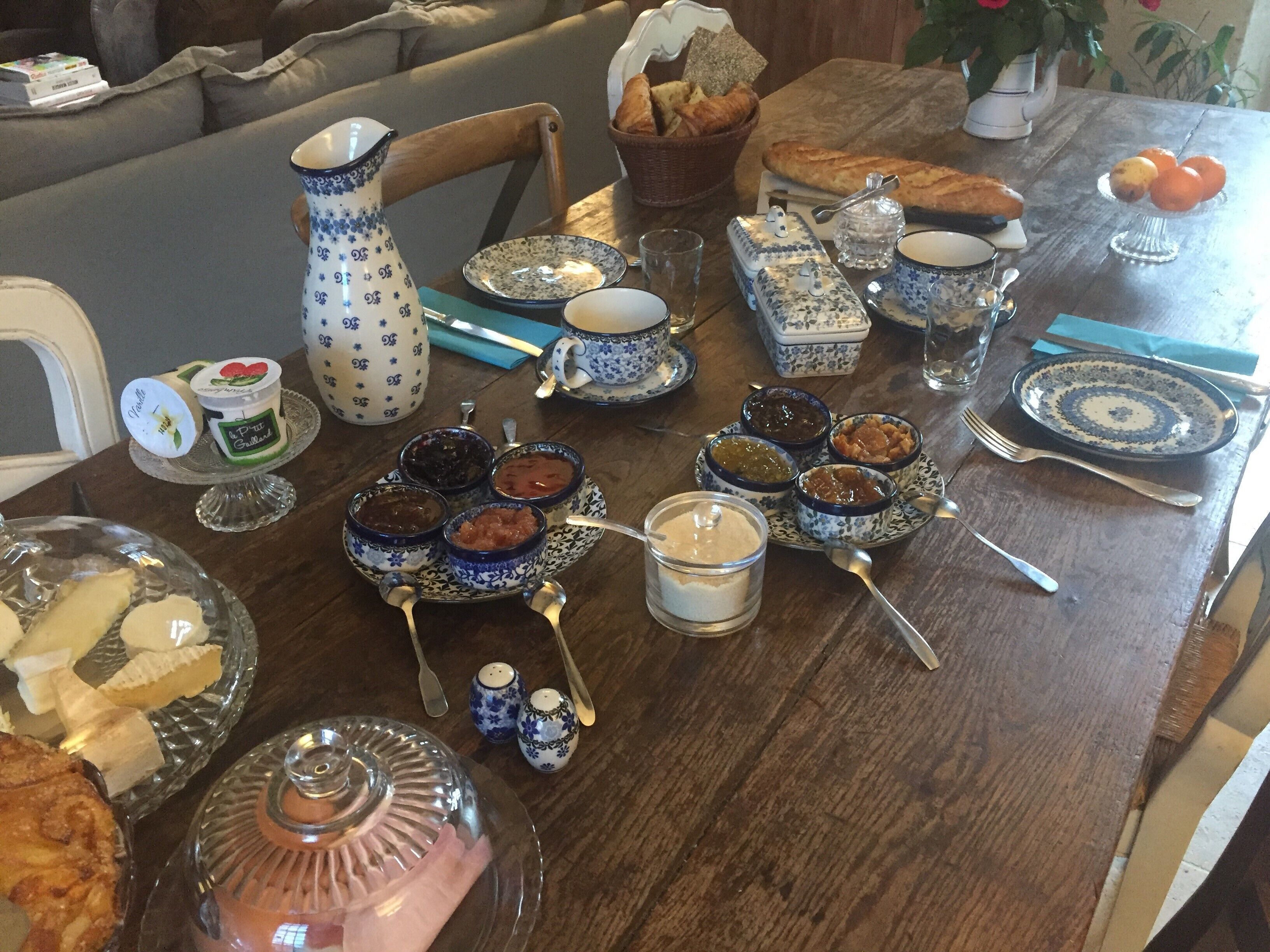 A dining table set with various dishes and condiments, including bread, fruit, and jars of preserves.