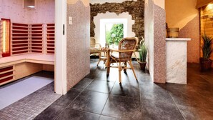 A spa area with a stone wall, a wooden bench, a wicker table with chairs, and a tiled floor. - La Ferme des Prés (Neuilly-en-Sancerre)