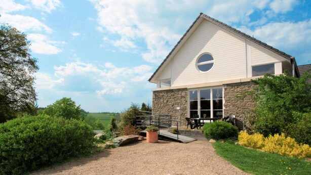 A two-story stone building with a white exterior, a circular window on the second floor, and a gravel driveway leading to a patio with outdoor seating. - La Ferme des Prés (Neuilly-en-Sancerre)