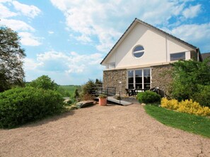 A two-story stone building with a white exterior, a circular window on the second floor, and a gravel driveway leading to a patio with outdoor seating. - La Ferme des Prés (Neuilly-en-Sancerre)