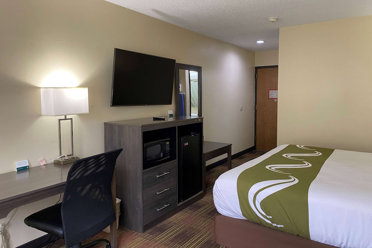 A hotel room with a bed, a desk with a chair, a television, a microwave, and a small refrigerator.