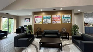 A modern living room with a black leather sofa, a coffee table, and a desk with a computer. There are four framed artworks on the wall and two side tables with decorative items.