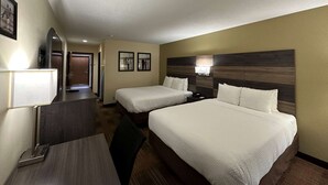 A hotel room with two beds, a desk, a chair, a lamp, and a mirror.