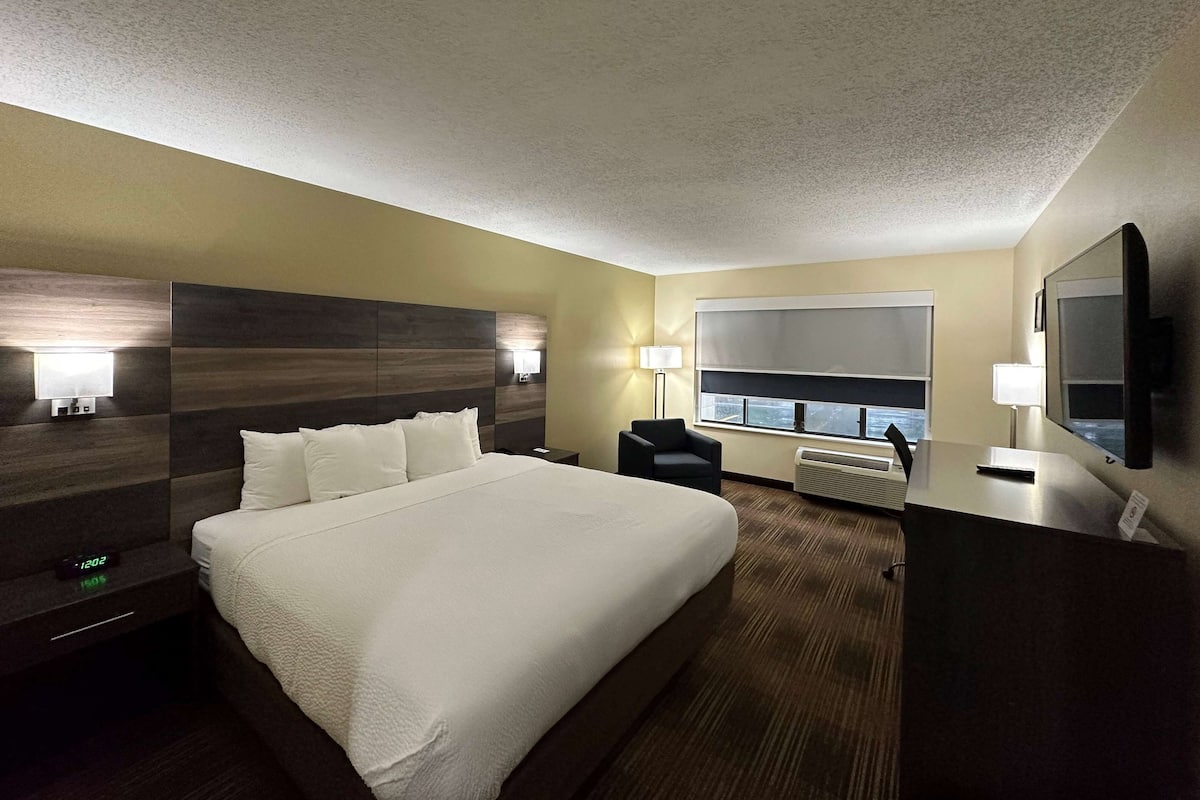 A hotel room with a large bed, bedside tables, a desk, a chair, a window, and a television.