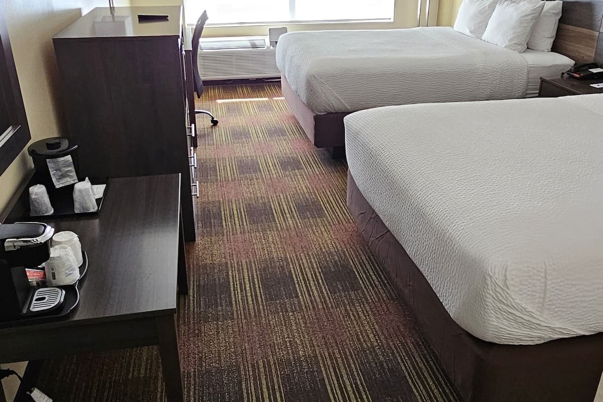 A hotel room with two beds, a desk with a chair, a TV, and a large window.