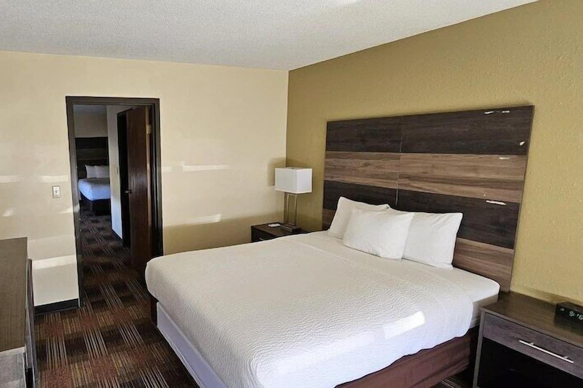 A hotel room with a bed, a TV, a desk, a lamp, and a door leading to another room.