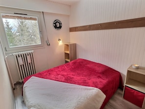 Ein Schlafzimmer mit Bett, Heizkörper, Fenster, einer an der Wand befestigten Schilder und einem Nachttisch.