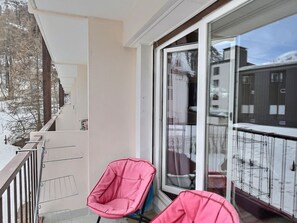 A balcony with two pink chairs, a glass door, and a view of buildings and trees.
