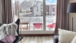 A room with a view of a snowy mountain, a balcony with chairs, and a large furry object on a chair. - 2-room apartment mountain view - 4 guests (Val-d'Isère)