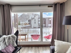 A room with a view of snowy mountains, a balcony with chairs, and a fur throw on a chair.