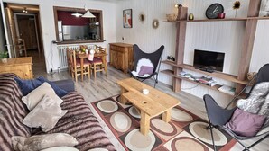 A living room with a sofa, a wooden coffee table, a dining table with chairs, a fireplace, and a television. - 2-room apartment mountain view - 4 guests (Val-d'Isère)