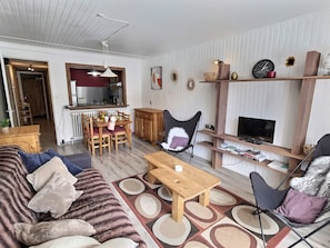 A living room with a sofa, a coffee table, a dining table with chairs, a fireplace, and a TV.