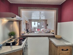A kitchen with a stove, sink, and cabinets, a dining area with chairs, and a view of the street.
