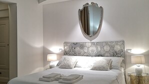 A neatly made bed with a patterned headboard, two bedside lamps, and a decorative mirror above it. - Eccelsoleccese (Lecce)