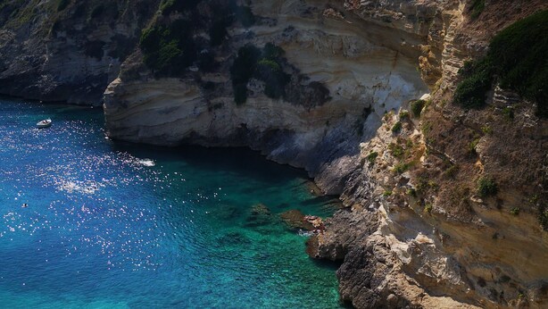 A beach with clear turquoise water, rocky cliffs, and people sunbathing under colorful umbrellas. - Eccelsoleccese (Lecce)
