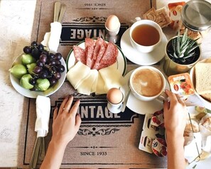 A breakfast setting with a plate of cheese, grapes, and salami, a cup of tea, a cup of coffee, and a thermos. - Eccelsoleccese (Lecce)