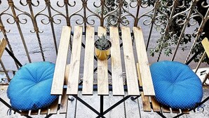 A wooden table with a potted plant and two blue cushions on a balcony with wrought iron railings. - Eccelsoleccese (Lecce)