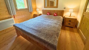 Camera da letto con rivestimento in legno, un letto, due comodini, uno specchio e una finestra con tende.