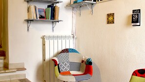 Une pièce avec un escalier, un radiateur, une bibliothèque, un miroir et une chaise dotée d’un coussin coloré.