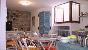Un coin repas avec des chaises en bois rustiques, une table recouverte d’une nappe verte et un espace cuisine doté d’étagères et d’appareils électroménagers.