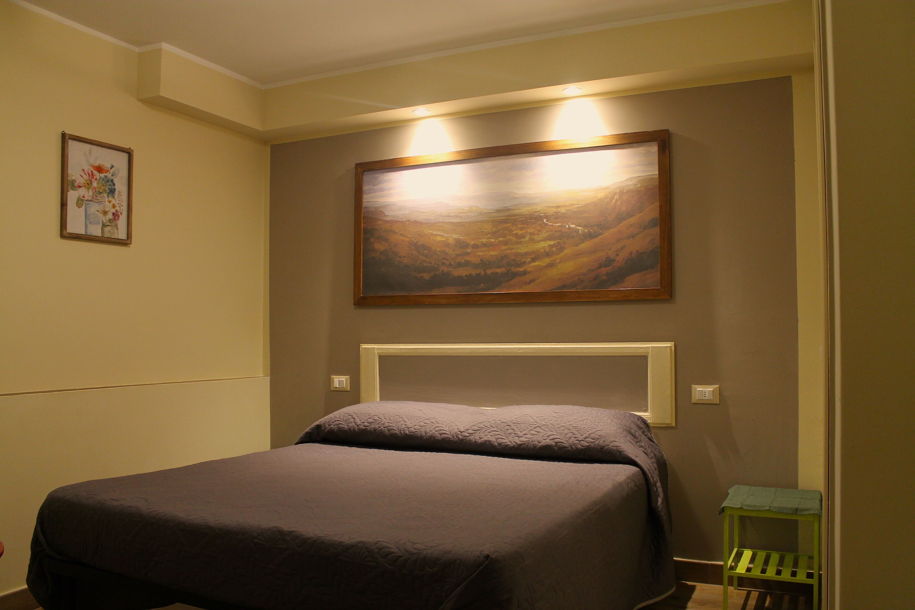 Una camera d'albergo con un letto, un quadro appeso al muro e un tavolino.