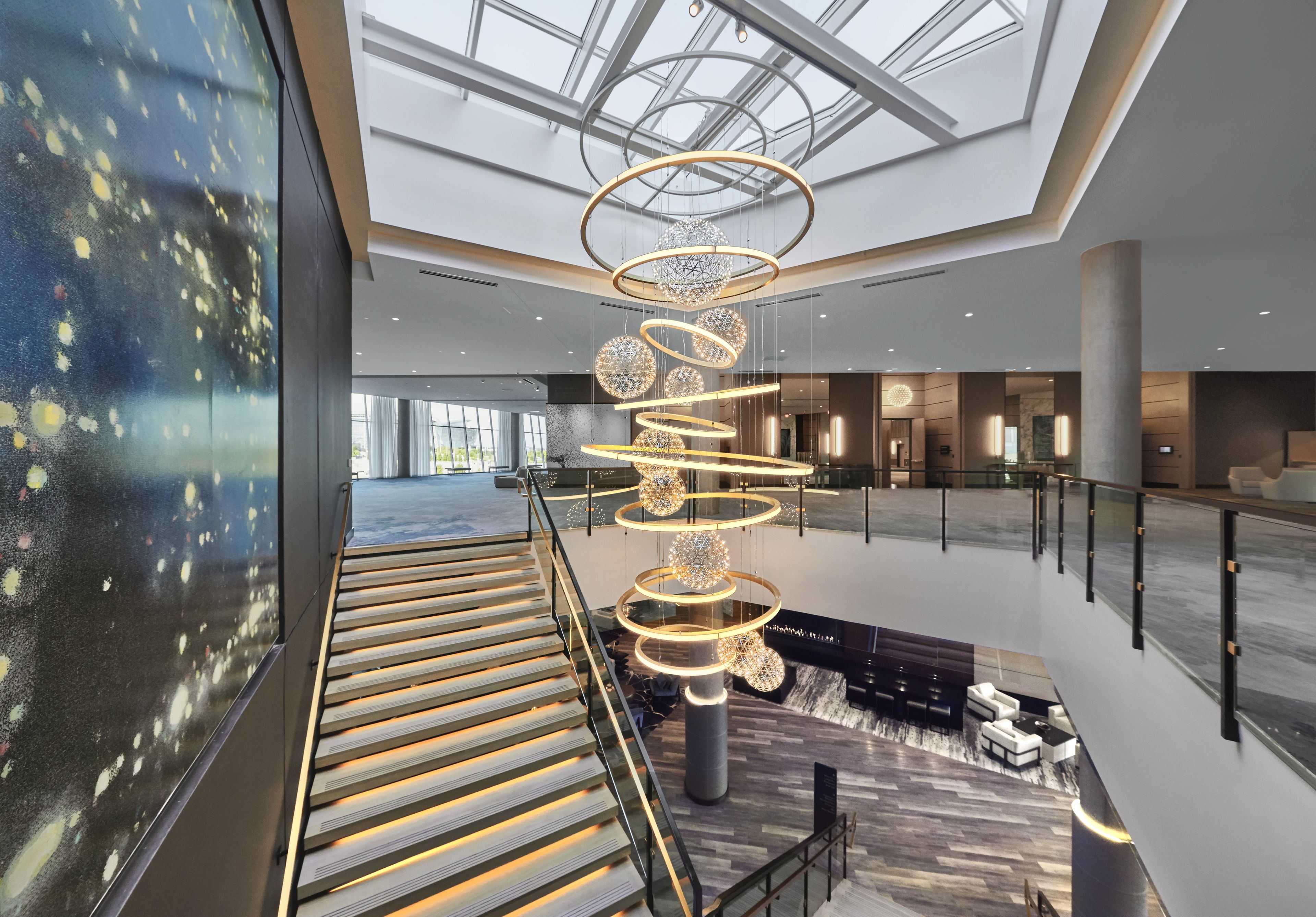 A spacious lobby with a modern chandelier, a staircase, and a high ceiling with skylights.