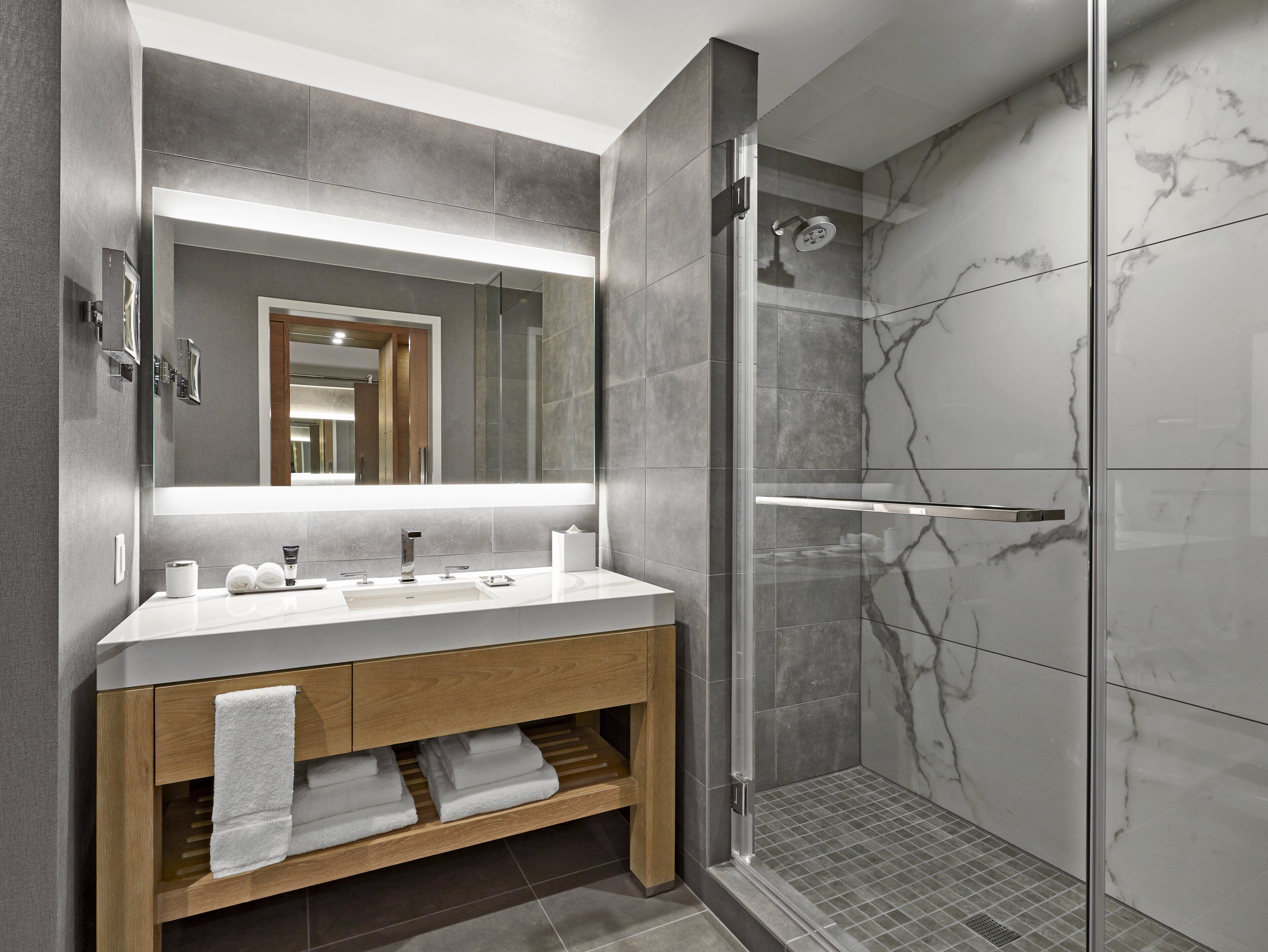 Un bany modern amb un moble de doble lavabo, una cabina de dutxa de vidre i parets de marbre.